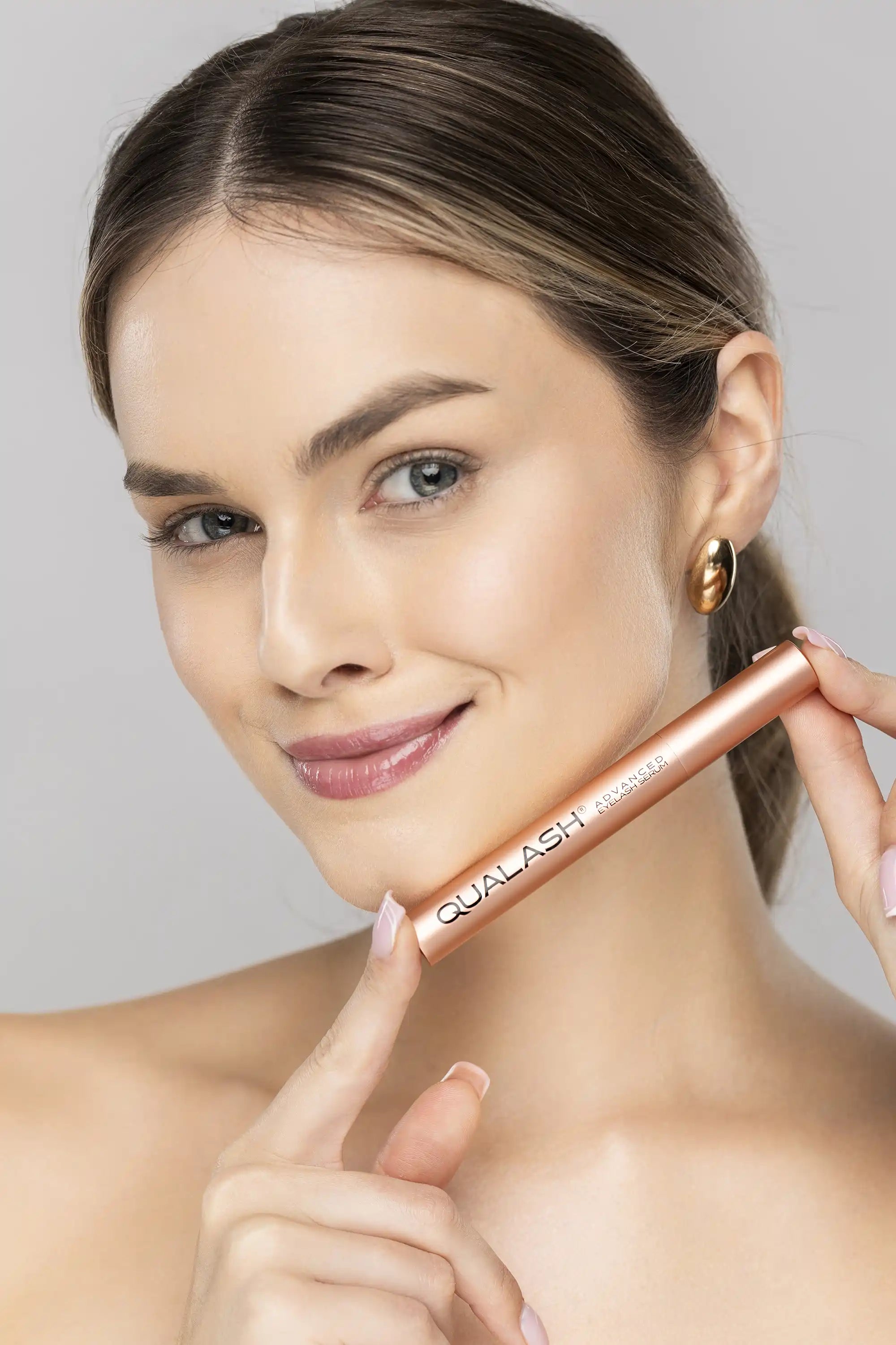 Smiling woman holding QUALASH Advanced Eyelash Serum before application